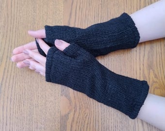 May include: A pair of black fingerless gloves made of knitted wool. The gloves are shown on a wooden surface.