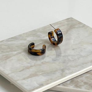 May include: A pair of brown and black tortoiseshell hoop earrings. The earrings are made of a smooth, glossy material and have a simple, elegant design.