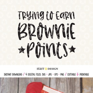 May include: A brown oven mitt with the text "Trying to Earn Brownie Points" in black lettering. The oven mitt is on a wooden surface with a box of Betty Crocker Fudge Brownie mix and a red spatula.