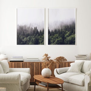 May include: Two framed photographs of a misty forest with tall evergreen trees. The photographs are hung on a white wall above a wooden cabinet and two white sofas.