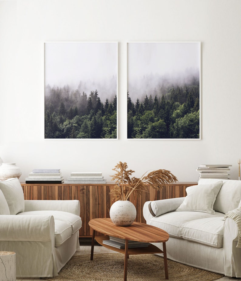 May include: Two framed photographs of a misty forest with tall evergreen trees. The photographs are hung on a white wall above a wooden cabinet and two white sofas.