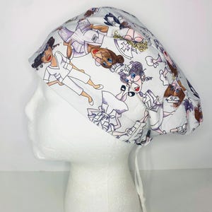 May include: A white scrub cap featuring a repeating pattern of cartoon nurses in various poses. The illustrations are in shades of black, white, and skin tones. The cap is tied at the back with white strings.