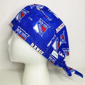 May include: A blue scrub cap featuring the New York Rangers logo and team name in white and red. The cap is patterned with the team's logo and name, and is tied at the back.