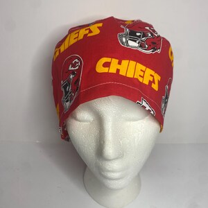 May include: Red and yellow Chiefs print scrub cap. The cap features the team's logo and the word "CHIEFS" in yellow. The cap is made of a soft, patterned fabric.
