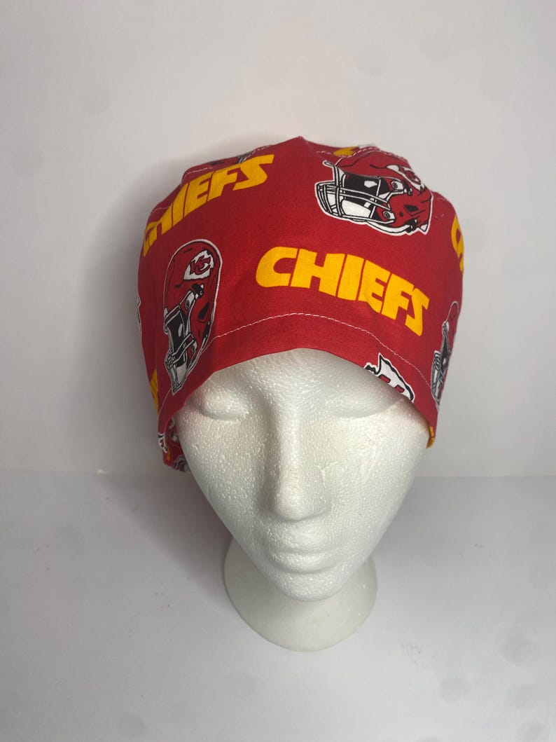 May include: Red and yellow Chiefs print scrub cap. The cap features the team's logo and the word "CHIEFS" in yellow. The cap is made of a soft, patterned fabric.