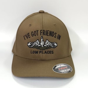 May include: A brown baseball cap with the text "I've got friends in low places" and a submarine graphic. The cap has a black brim and a white Flexfit logo.