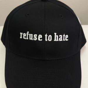May include: A black baseball cap with white embroidered text that reads "refuse to hate".