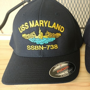May include: Two black baseball caps with embroidered navy blue patches. The patches feature the text "USS MARYLAND" and "SSBN-738" with a yellow submarine graphic.