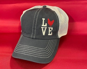 May include: A navy blue and white mesh trucker hat with the word "LOVE" embroidered on the front, with a red chicken graphic in the "O".