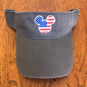 May include: A gray visor with an embroidered American flag Mickey Mouse design.