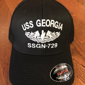 May include: Black baseball cap with white embroidered text "USS GEORGIA" and "SSGN-729" and a white submarine emblem. The cap has a black Flexfit label.