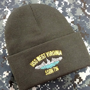 May include: Black knit beanie with a yellow embroidered patch that reads "USS WEST VIRGINIA SSBN 736". The patch features a blue submarine with three yellow figures on top.