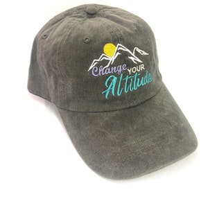 K&ouml;nnte beinhalten: Eine schwarze Baseballkappe mit einem gestickten Design aus Bergen, einer Sonne und dem Text "Change Your Altitude".