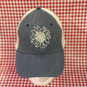 May include: A blue and white baseball cap with a white embroidered sunflower design. The cap has a mesh back and a curved brim.