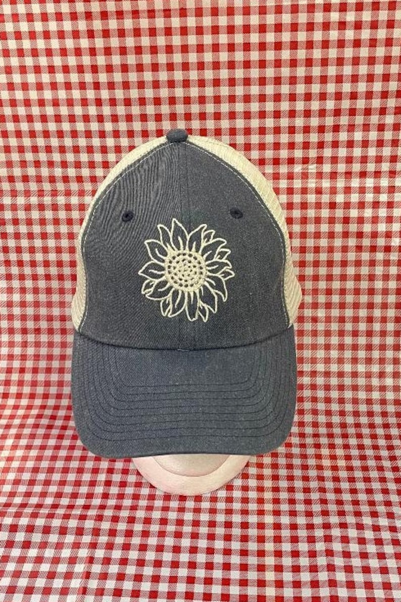 May include: A blue and white baseball cap with a white embroidered sunflower design. The cap has a mesh back and a curved brim.