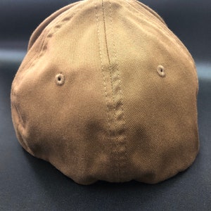 May include: A tan baseball cap with a curved brim. The cap has a button on top and two small ventilation holes on the sides. The fabric has a textured appearance.