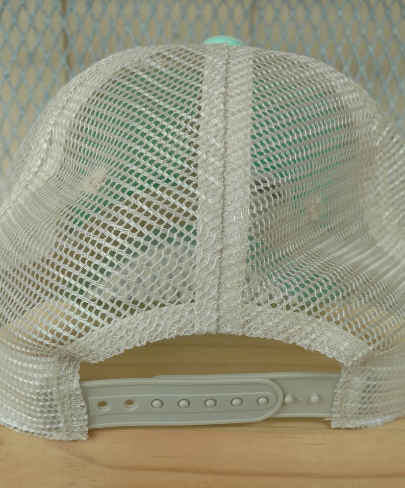 May include: A white mesh trucker hat with a light green underside and a plastic adjustable strap.