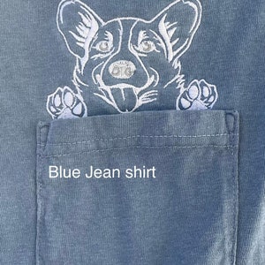 May include: A blue jean shirt with a white embroidered image of a dog peeking out of the pocket. The text "Blue Jean shirt" is embroidered below the dog.