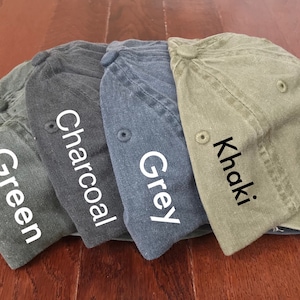 K&ouml;nnte beinhalten: Vier Baseballkappen in verschiedenen Farben: Gr&uuml;n, Anthrazit, Grau und Khaki. Die Kappen sind in einer Reihe angeordnet, wobei die gr&uuml;ne Kappe links und die Khaki-Kappe rechts ist.