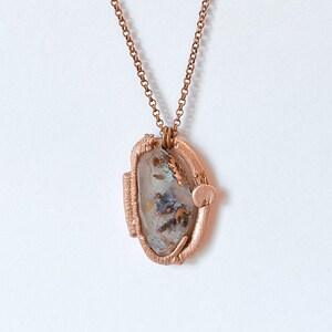 May include: A rose gold necklace with a unique pendant featuring a clear, agate-like stone with brown and gold flecks. The stone is set in a rose gold wire frame.
