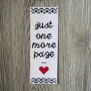 Może przedstawiać: Biała zakładka z czarnym haftem krzyżykowym z napisem "Just one more page" i czerwonym sercem.