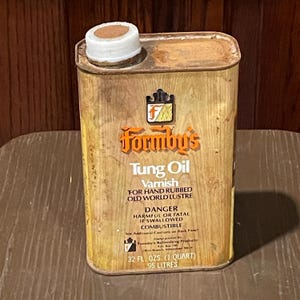 May include: A vintage can of Formby's Tung Oil Varnish for hand rubbed old world lustre. The can is rusty and has a white lid. The label is yellow and orange with black text. It reads "Formby's Tung Oil Varnish for Hand Rubbed Old World Lustre. Danger Harmful or Fatal if Swallowed. Combustible. 32 fl. ozs. (1 quart) .95 litres."