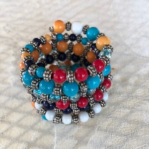 May include: A multi-strand bracelet with turquoise, red, orange, white, and black beads. The beads are separated by silver spacers.