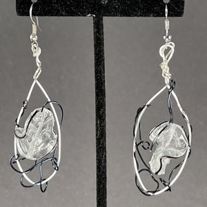 May include: A pair of silver earrings with clear plastic pieces suspended in a black wire cage.