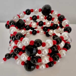 May include: A multi-strand bracelet featuring a spiral design. The bracelet is composed of white, black, and red beads. The beads are a mix of round and faceted shapes, creating a visually appealing accessory.