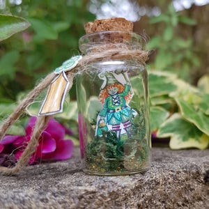 May include: A small glass bottle with a cork stopper, filled with green moss, glitter, and a paper cutout of a leprechaun wearing a green hat and holding a pot of gold.