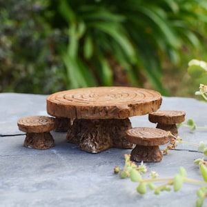 May include: A miniature fairy garden furniture set, featuring a round table and three stools, all crafted from a wood-like material. The table has a textured surface with concentric circles, and the stools have a similar design. The set is designed for outdoor use.