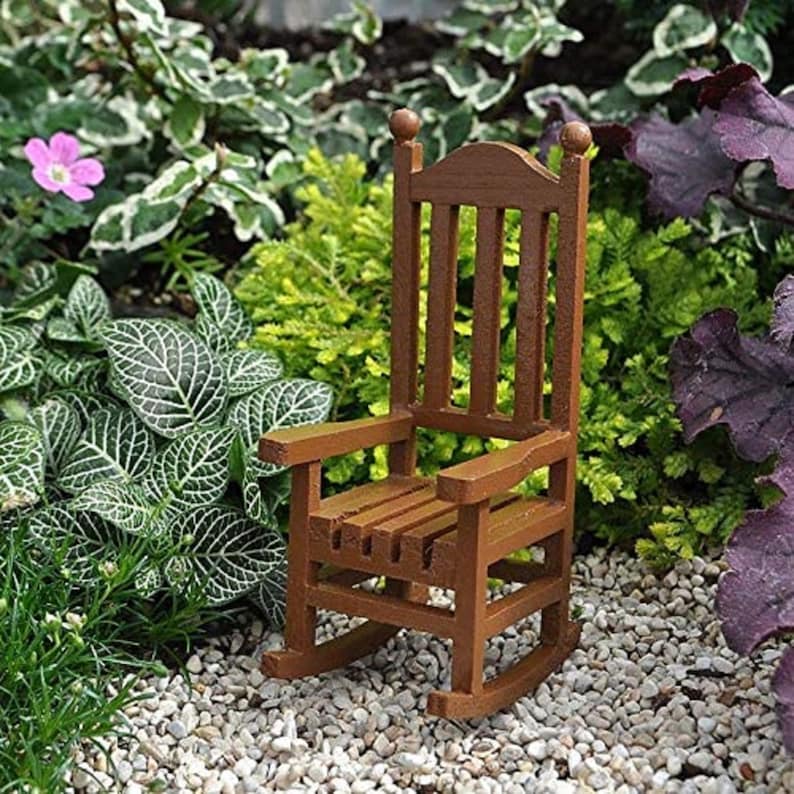 May include: A miniature wooden rocking chair with a brown finish. The chair is sitting on a bed of small white stones.