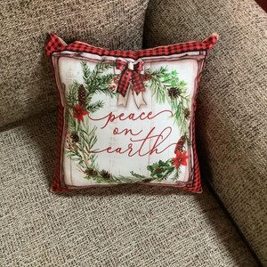 May include: Red and white plaid pillow with a green wreath and the words "peace on earth" printed on it.