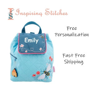 May include: A light blue quilted backpack with a bee and flower embroidery design. The backpack has a flap with a blue fabric panel that says "Emily" in white embroidery. The backpack has a zippered pocket and a small bee charm.