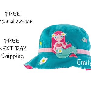 May include: A turquoise blue bucket hat with a pink trim and a mermaid applique. The mermaid is pink and green with a white flower in her hair. The hat has a white daisy applique and the name "Emily" is embroidered on the front.