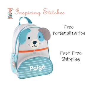 May include: A blue and gray dog-shaped backpack with a white front pocket and a blue and white striped bottom pocket. The backpack has a name tag that says "Paige".