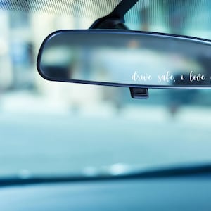 May include: A rearview mirror with the words "drive safe, i love you" written on it in white lettering.