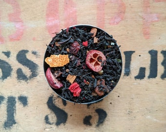 May include: A close-up of a black tea blend with dried fruit pieces, including cranberries, orange peel, and cinnamon sticks. The tea is in a small metal bowl.