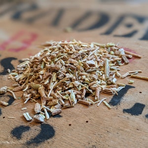 May include: A close-up of a pile of dried herbs, likely for tea or herbal remedies. The herbs are a mix of light brown, beige, and green, and appear to be finely chopped or shredded.