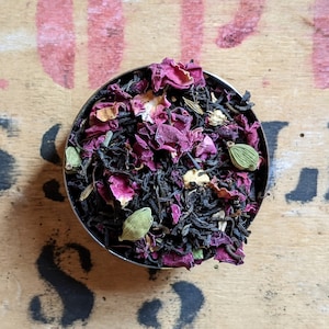 Könnte beinhalten: Nahaufnahme einer Schale gefüllt mit einer Mischung aus schwarzem Tee, Rosenblüten und grünen Kardamomkapseln.