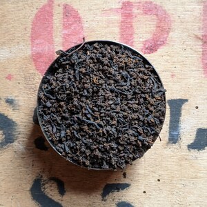 May include: A close-up of a small metal container filled with loose black tea leaves.