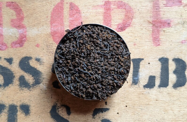 May include: A close-up of a small metal container filled with loose black tea leaves.