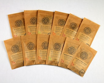 May include: A collection of 14 brown paper tea bags with different tea flavours printed on the front. The tea flavours include Winter Berry, Caramel Chili, Mint Blend, Ginger, Pink Grapefruit, Root Chai, Rooibos Chai, Citrus Herbal, Tropical, English Garden,  Rhubarb Custard, and Rooibos Earl Grey.