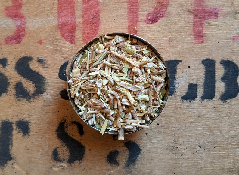 May include: A small metal bowl filled with dried herbs and roots. The herbs are a mix of light brown, beige, and green.