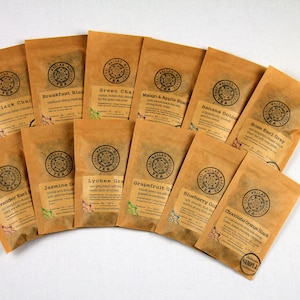 May include: A variety of loose leaf tea bags in brown paper packaging with different tea flavors printed on each bag. The tea flavors include Black Chai, Breakfast Blend, Green Chai, Mango & Apple Black, Banana Colada, Rose Earl Grey, Lavender Earl Grey, Jasmine Green, Lychee Green, Grapefruit Green, Blueberry Oolong, and Chocolate Orange Black.