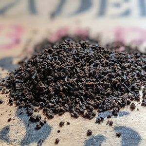 May include: A close-up of a pile of loose leaf black tea on a wooden surface.