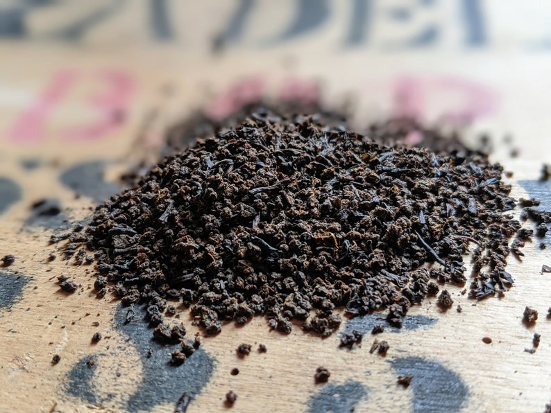 May include: A close-up of a pile of loose leaf black tea on a wooden surface.