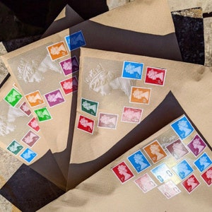 May include: Three brown envelopes with colorful stamps featuring a portrait of a woman. The stamps are arranged in a pattern on the envelopes.