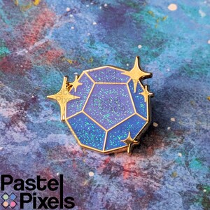 May include: A blue and purple gemstone enamel pin with gold accents. The pin features a geometric design with glitter details and star-shaped embellishments. The pin is set against a colorful, galaxy-themed background.