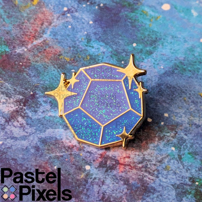 May include: A blue and purple gemstone enamel pin with gold accents. The pin features a geometric design with glitter details and star-shaped embellishments. The pin is set against a colorful, galaxy-themed background.